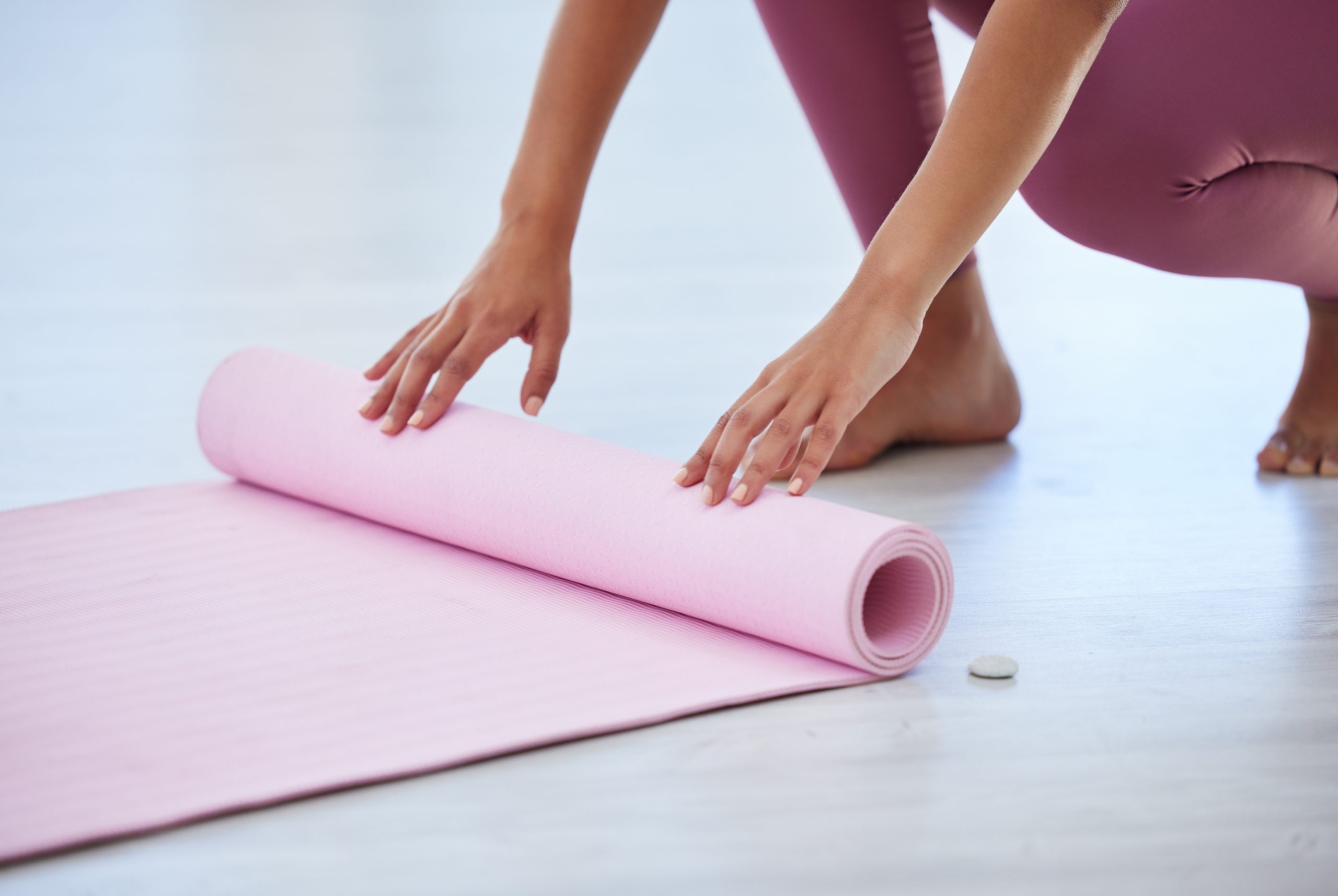 Hands, rolling and yoga mat with person on floor of studio apartment, getting ready for holistic routine. Exercise, fitness and preparation with yogi person closeup in home for pilates or wellness.